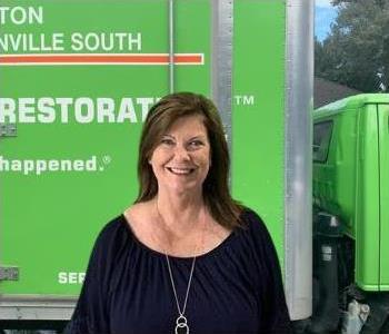 female employee with brown hair and a black shirt in front of a green SERVPRO truck