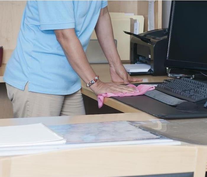 Alt Image Tag: female wiping a desk and computer with a pink rag
